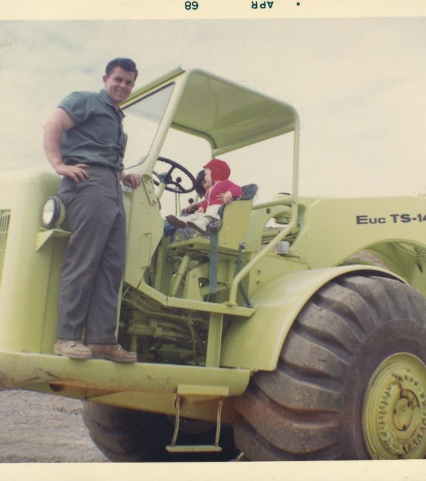 Two large dump trucks drive on a dirt construction site.