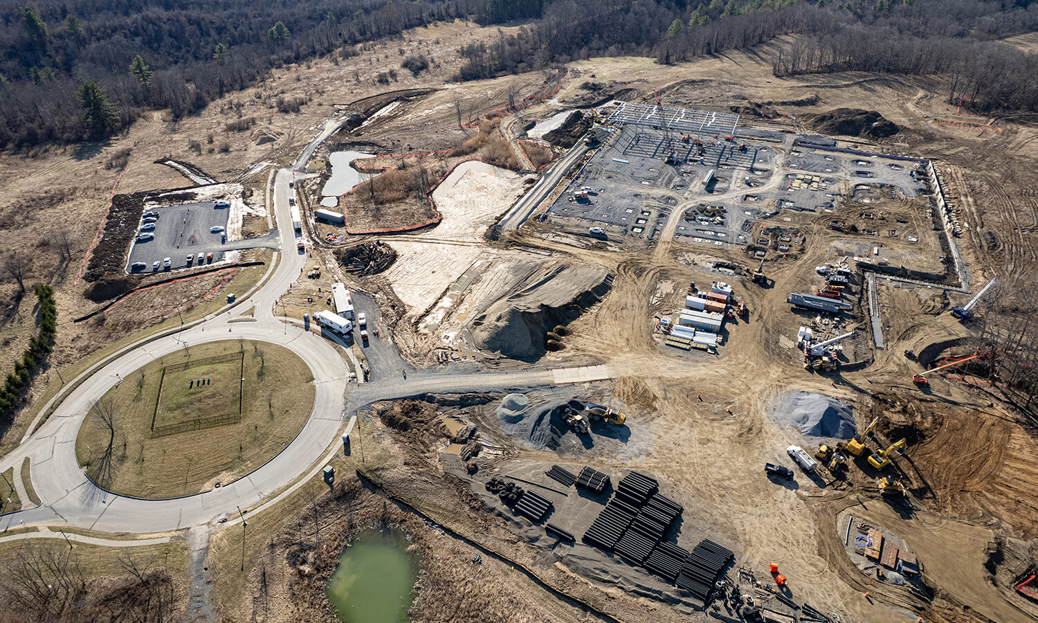 Aerial view: early-stage buildings, construction vehicles, roundabout, barren land.