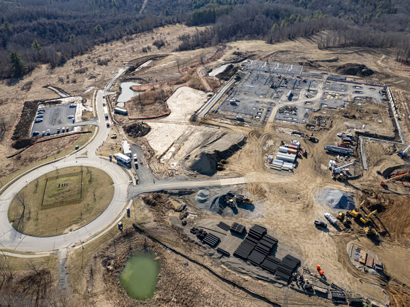 Aerial view: early-stage buildings, construction vehicles, roundabout, barren land.