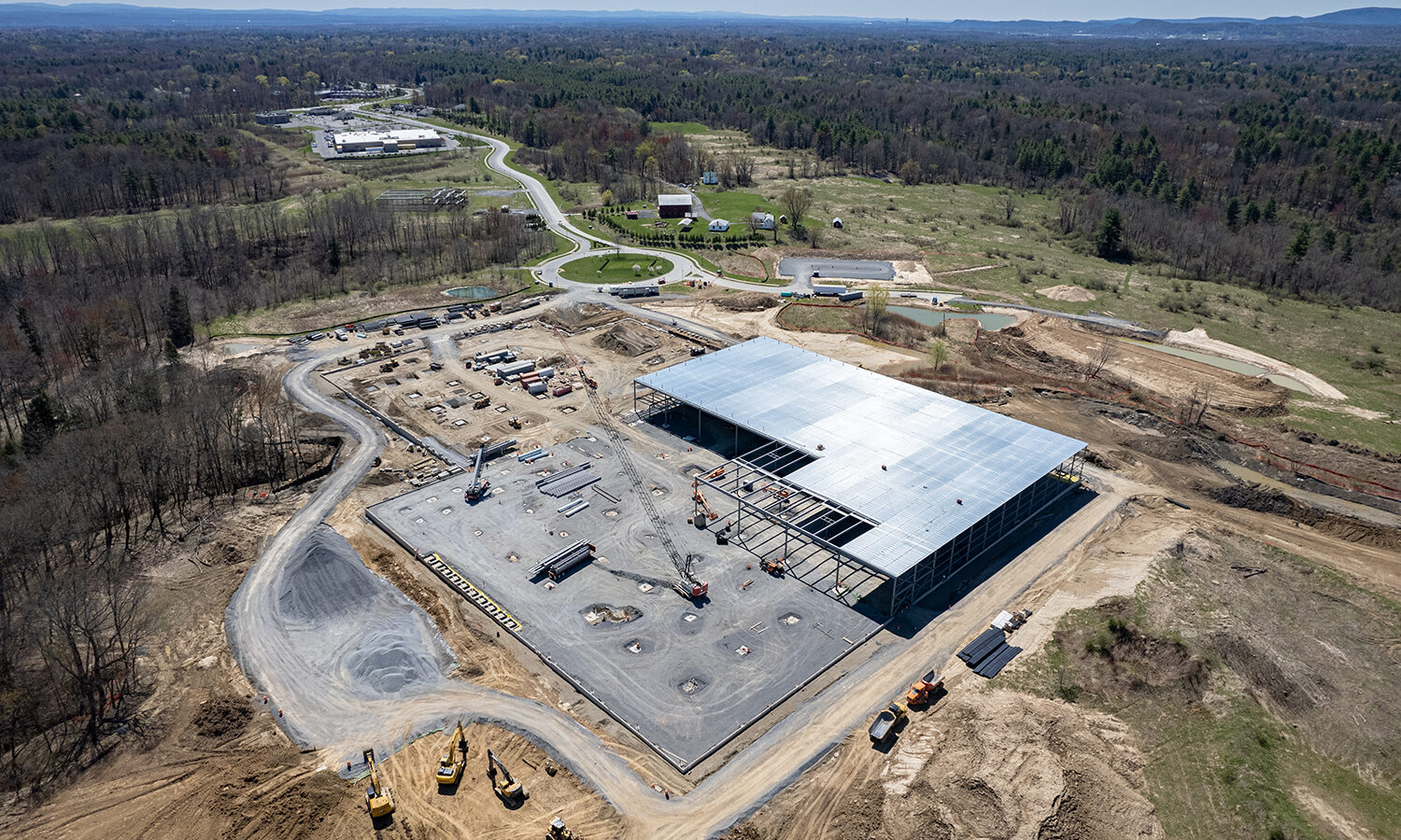 Aerial view: building under construction amid vehicles, forest behind.