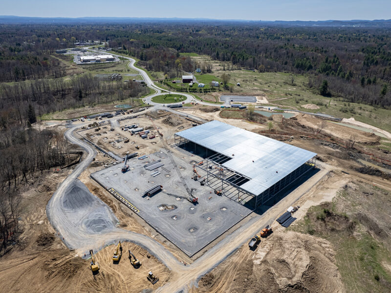 Aerial view: building under construction amid vehicles, forest behind.