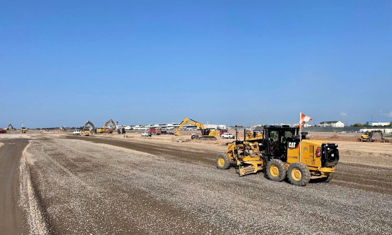 Construction vehicles work on gravel site under clear blue sky.