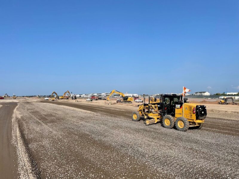 Construction vehicles work on gravel site under clear blue sky.
