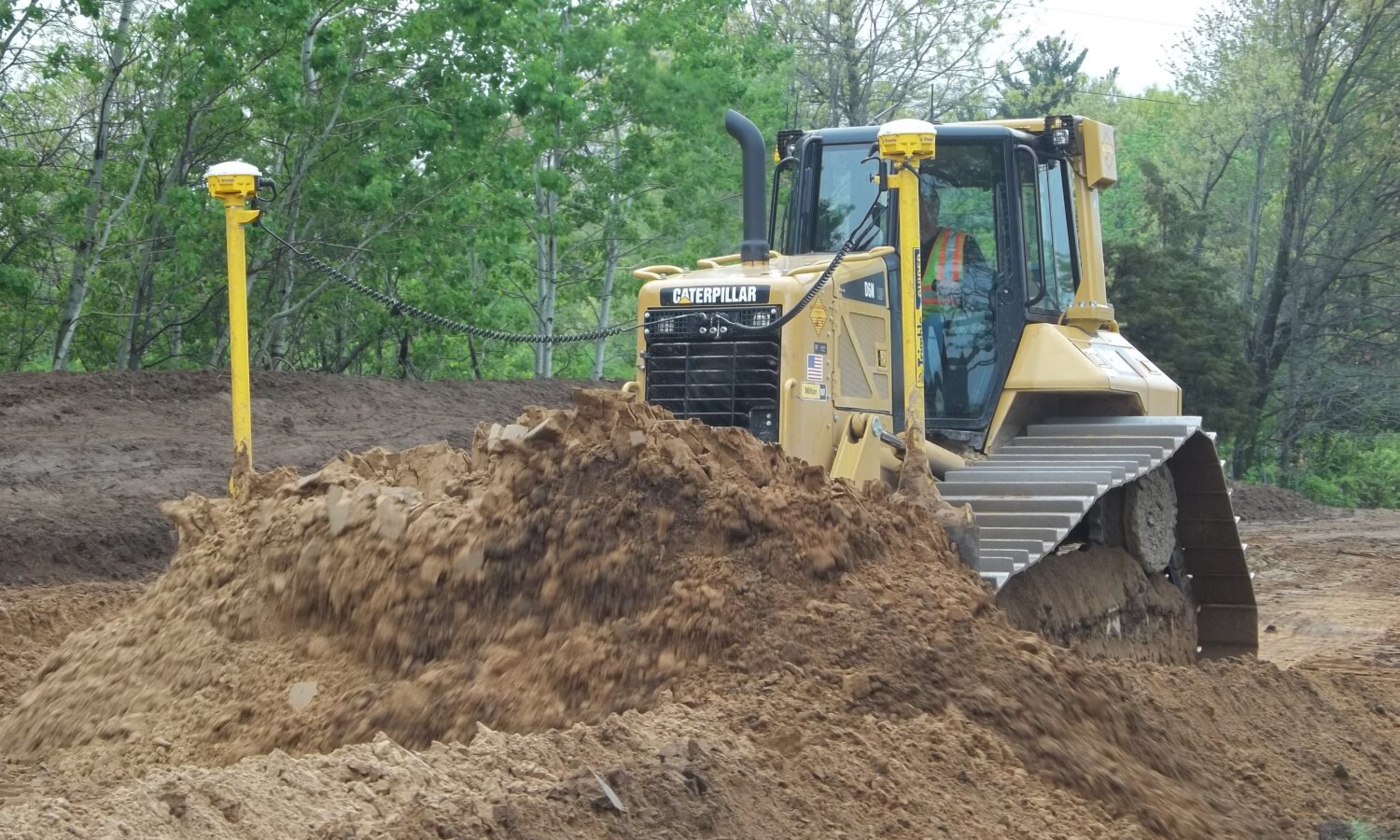 Yellow Caterpillar bulldozer pushes dirt at tree-lined construction site.