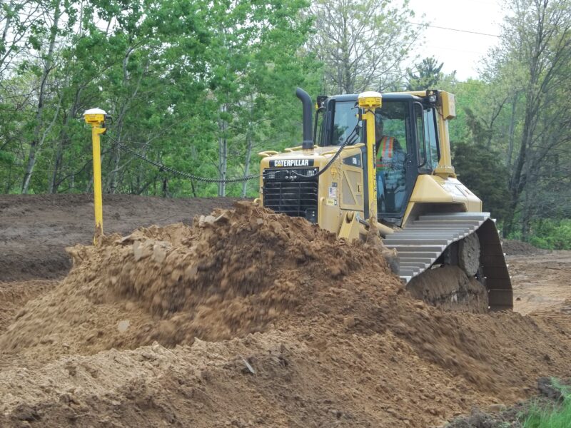 Yellow Caterpillar bulldozer pushes dirt at tree-lined construction site.