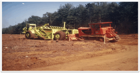 Two large dump trucks drive on a dirt construction site.