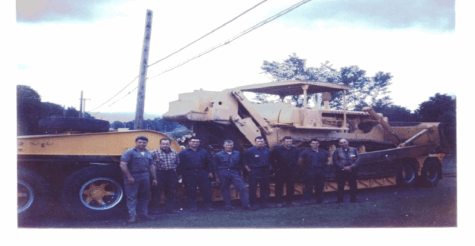 Two large dump trucks drive on a dirt construction site.