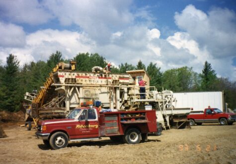 Two large dump trucks drive on a dirt construction site.