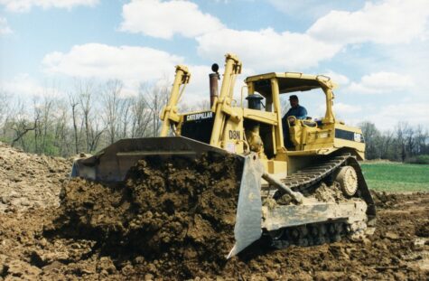 Two large dump trucks drive on a dirt construction site.