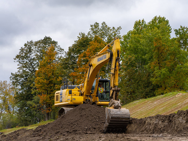 Yellow Komatsu excavator moves dirt amid autumn trees.