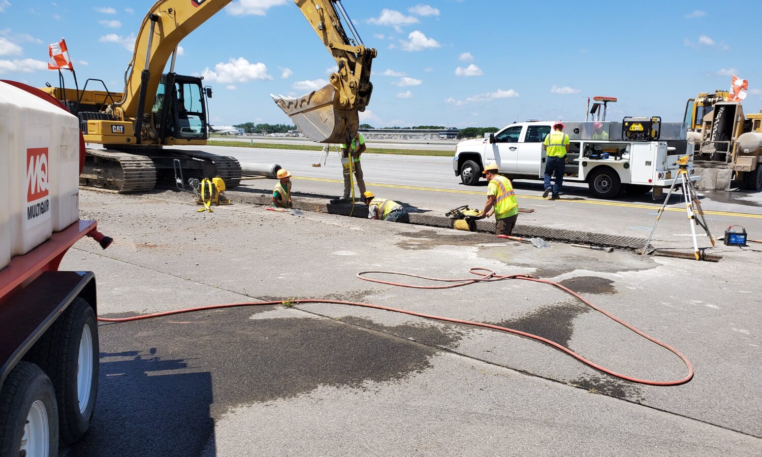Construction workers repair pavement beside machinery on a clear day.