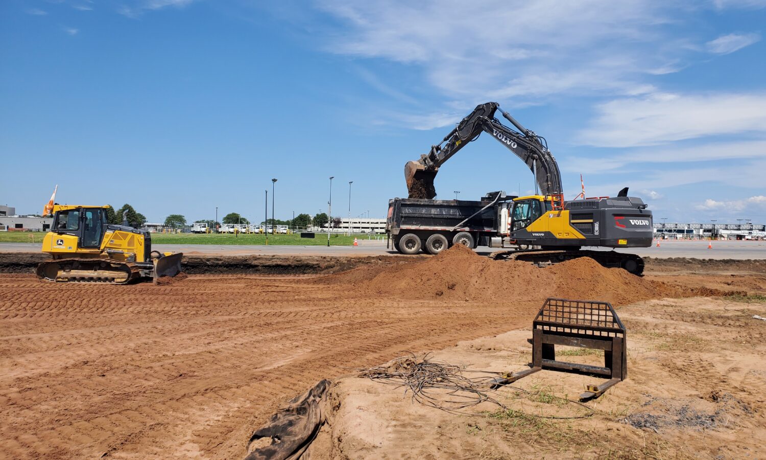 Excavator loads dump truck; bulldozer works nearby under clouds.