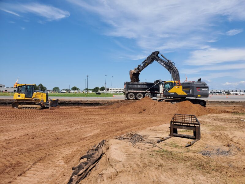 Excavator loads dump truck; bulldozer works nearby under clouds.