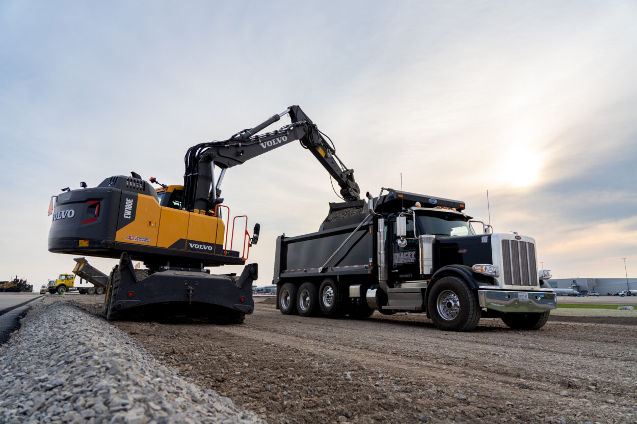 Volvo excavator loads gravel into black dump truck.