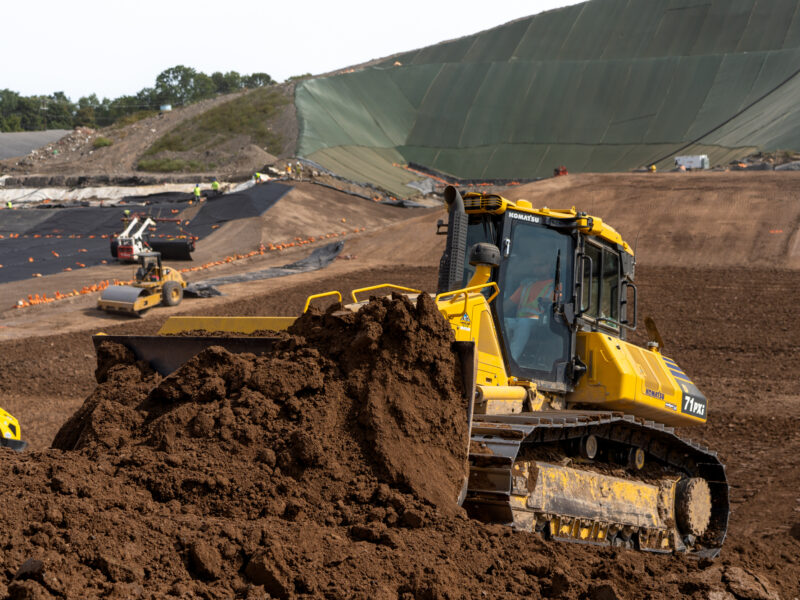 Yellow bulldozer moves soil with machinery and tarped slopes behind.