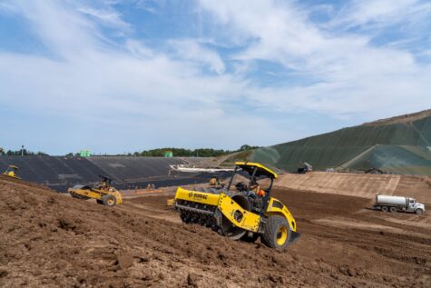 Two large dump trucks drive on a dirt construction site.