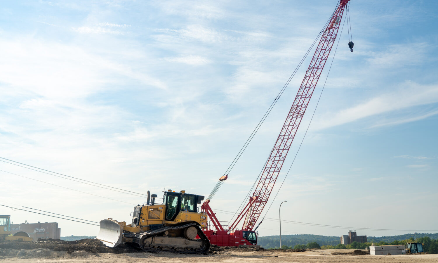 Bulldozer and red crane on construction site under clouds.