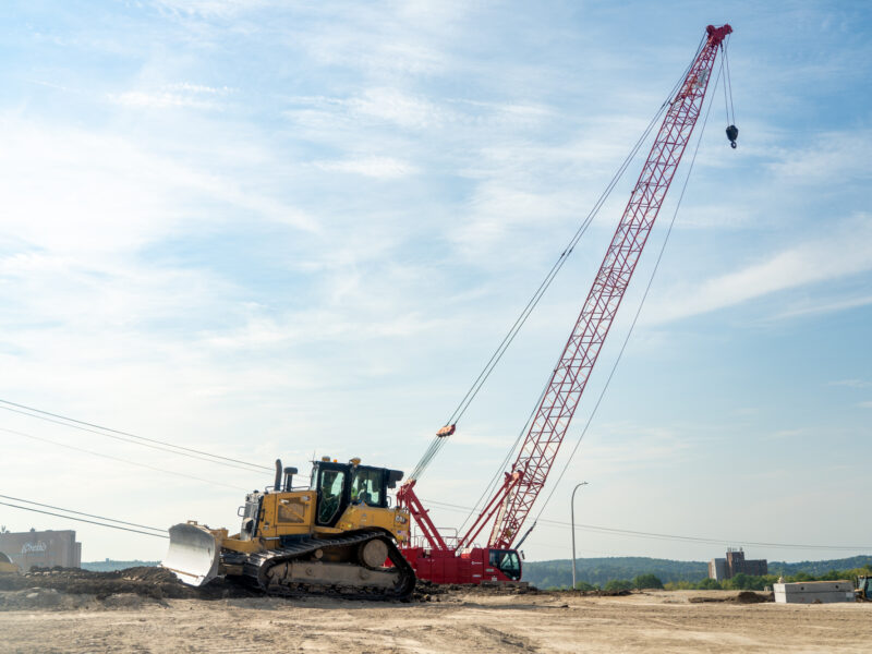 Bulldozer and red crane on construction site under clouds.