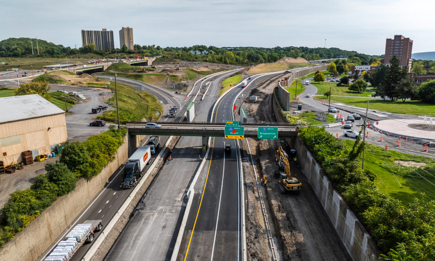 Aerial view: highway construction, vehicles, equipment, overpass, green signs.