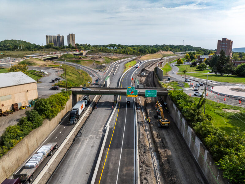 Aerial view: highway construction, vehicles, equipment, overpass, green signs.