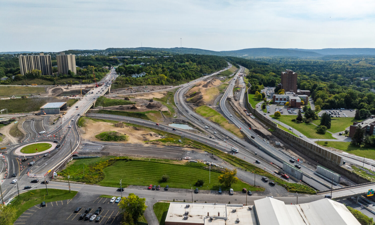 Aerial view of highway construction with nearby buildings and greenery.