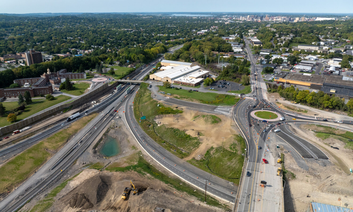 Aerial view: highway roundabout, buildings, vehicles, green spaces.