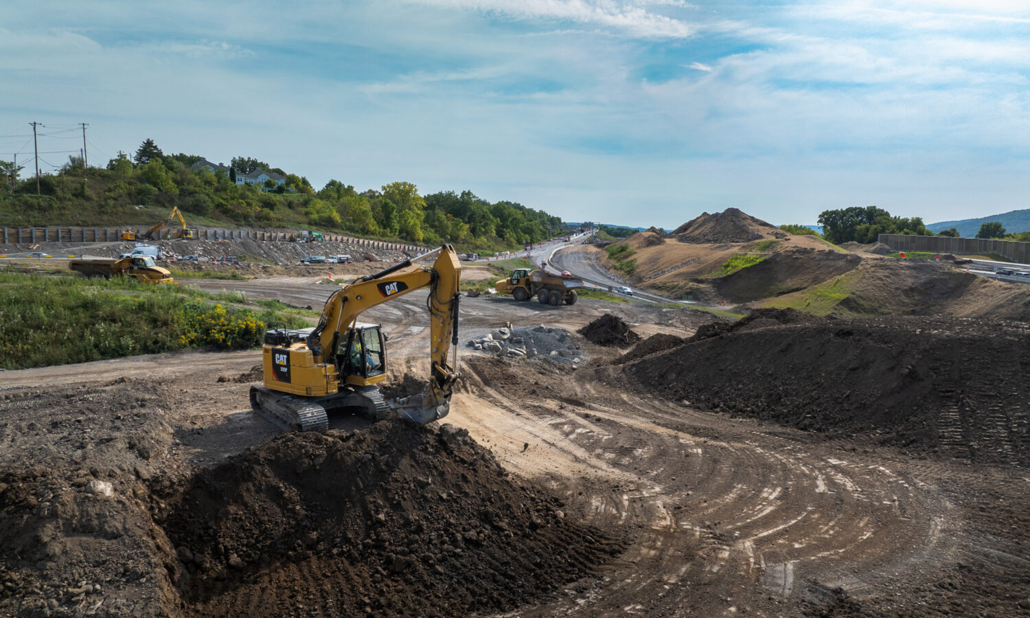 Excavator moves dirt beside a partially built road.