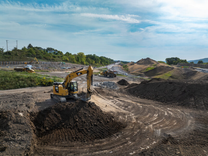 Excavator moves dirt beside a partially built road.