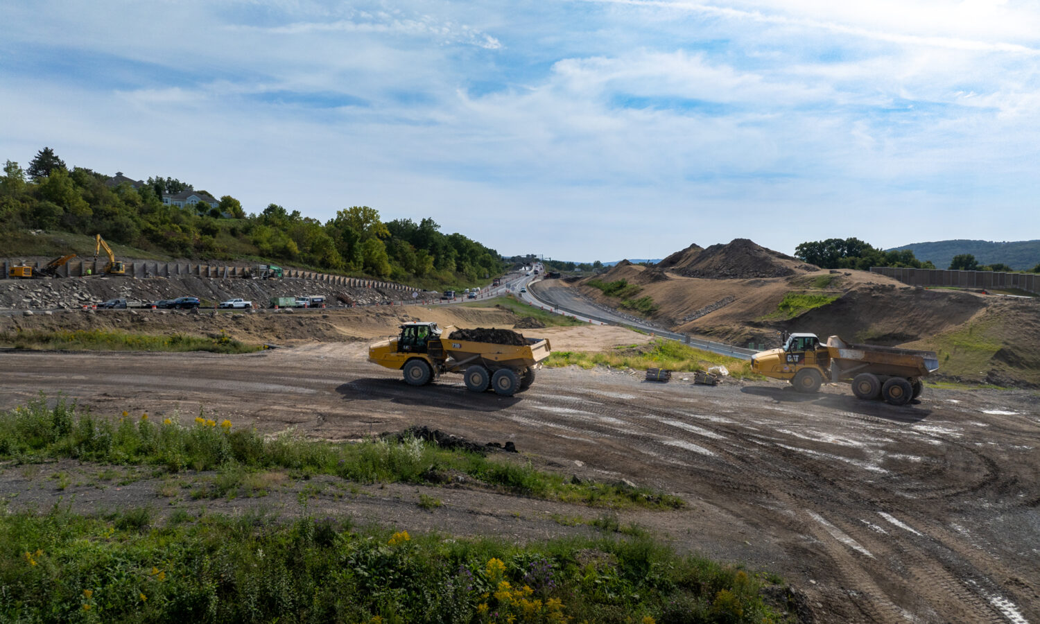 Two dump trucks drive on a dirt road near construction.