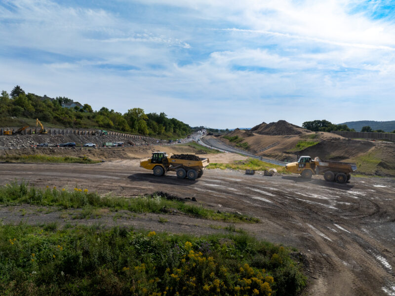 Two dump trucks drive on a dirt road near construction.
