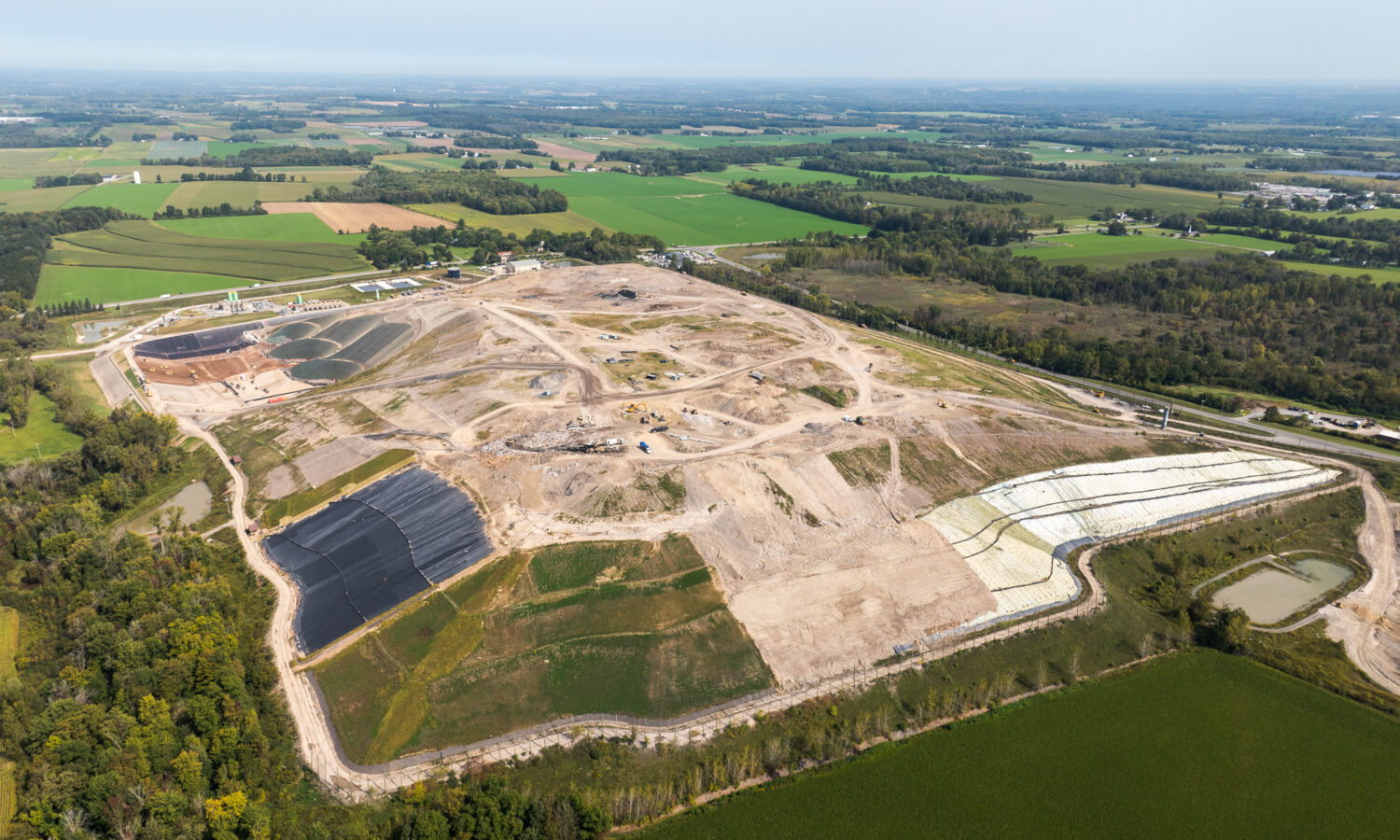 Aerial view of landfill under construction near farmland and trees.