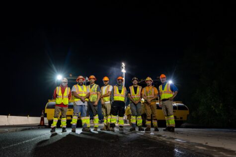 Two large dump trucks drive on a dirt construction site.