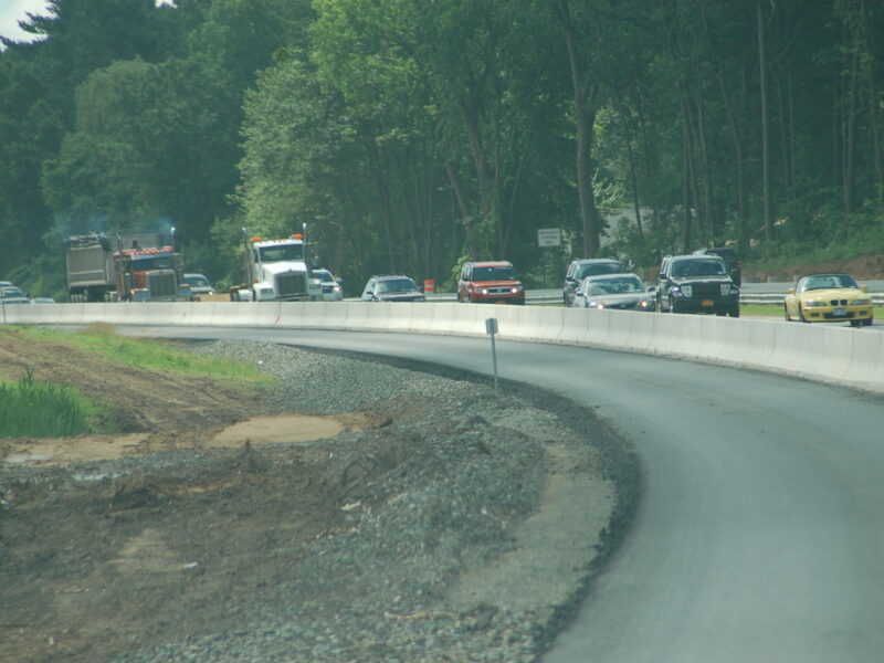 Cars and trucks on divided highway; construction on left side.