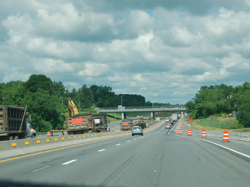 Highway construction left; cars drive both ways under cloudy sky.