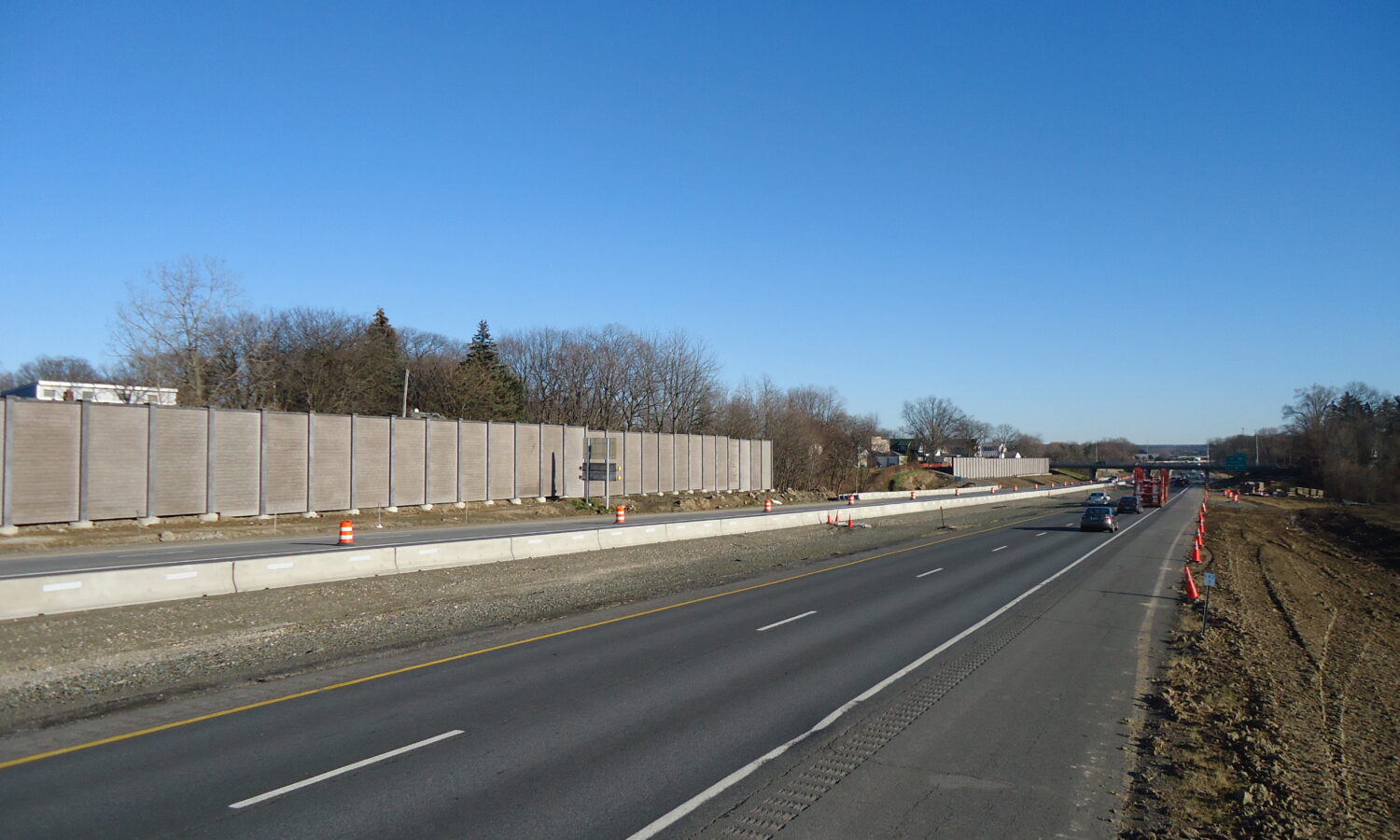 Divided highway under construction, barriers, cones, few cars driving.
