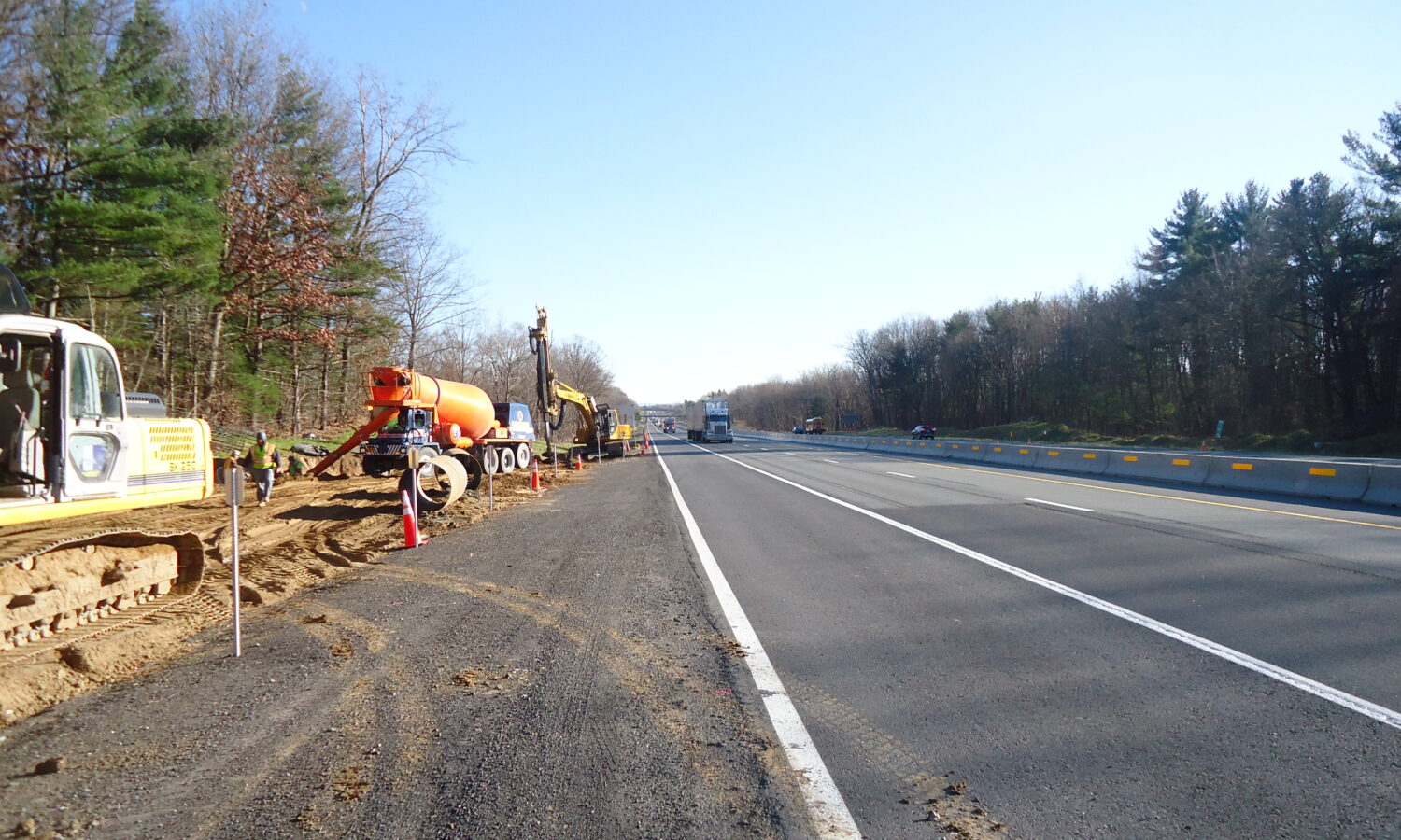 Construction vehicles line the highway behind traffic barriers under clear skies.