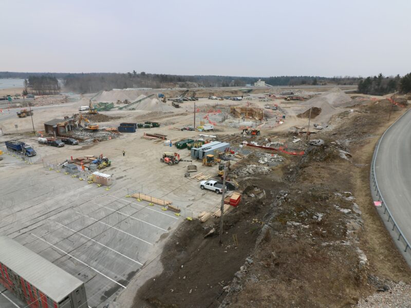 Construction site with machinery, dirt piles, and empty parking lot.