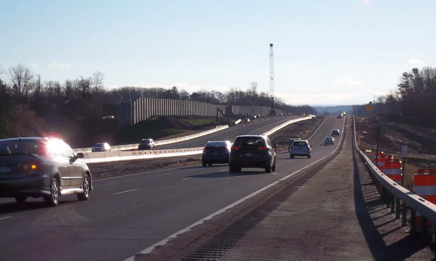 Cars on highway, sound barrier left, crane ahead, clear sky.