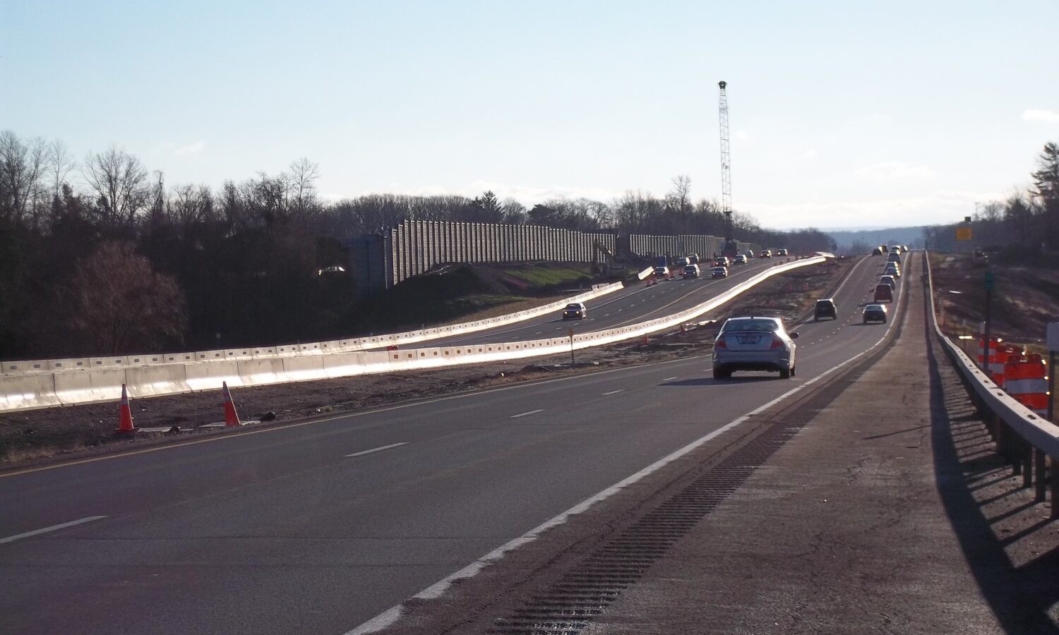 Cars drive on highway past construction zone under clear sky.
