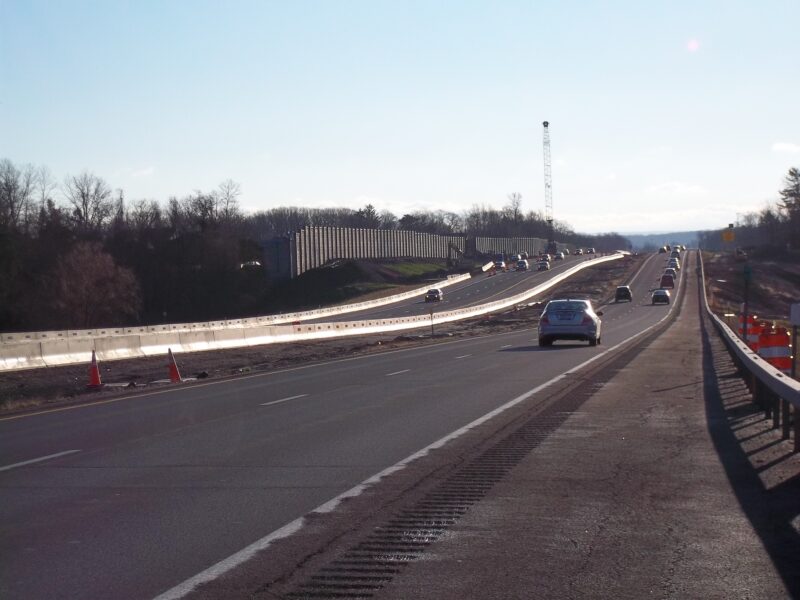 Cars drive on highway past construction zone under clear sky.