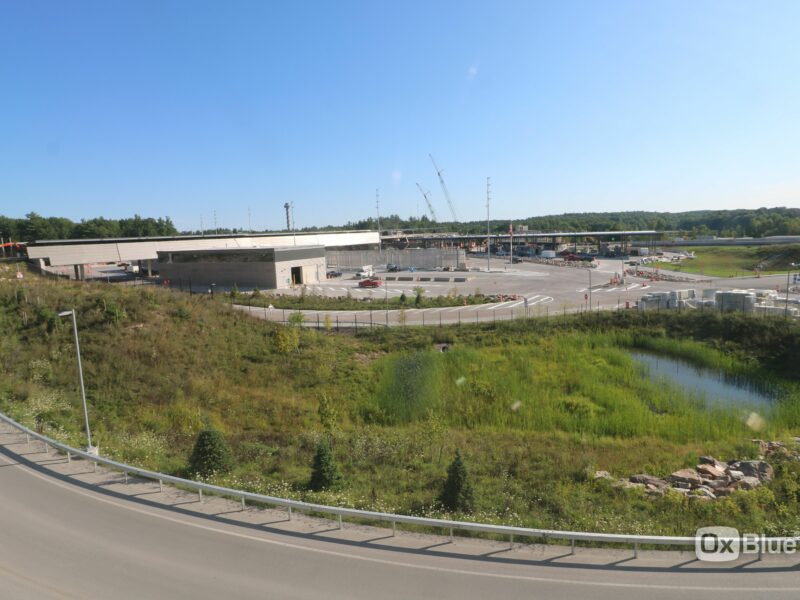 Construction site with cranes, vehicles, greenery, and pond.