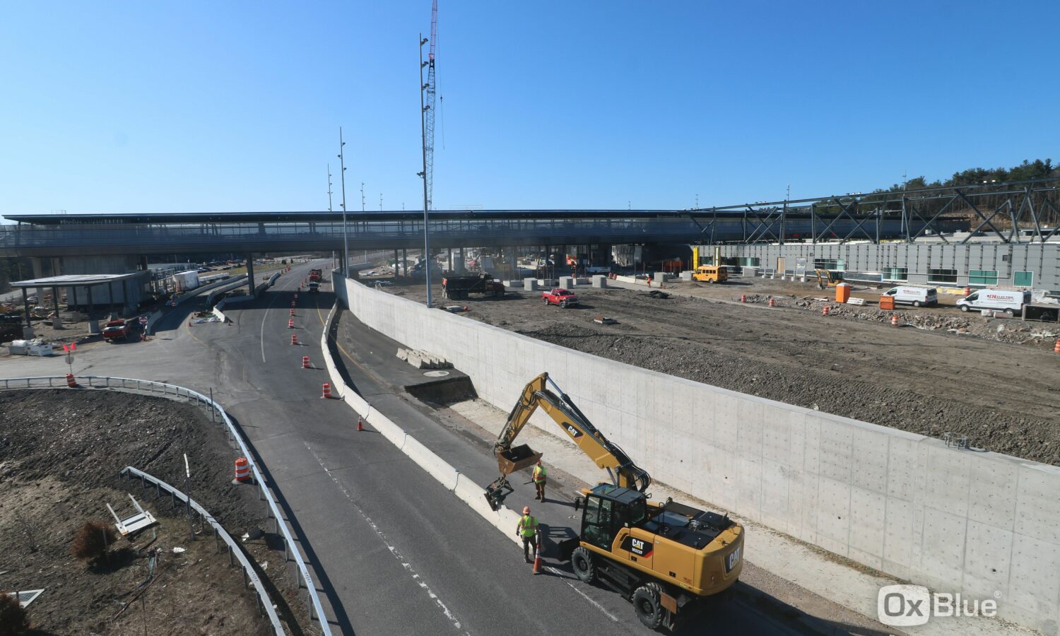 Excavator and workers at highway construction site near bridge.