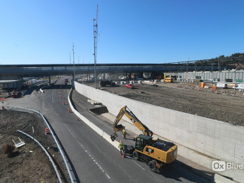 Excavator and workers at highway construction site near bridge.