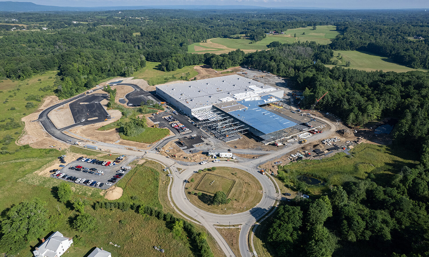 Aerial view: large industrial building construction amid trees, roundabout.