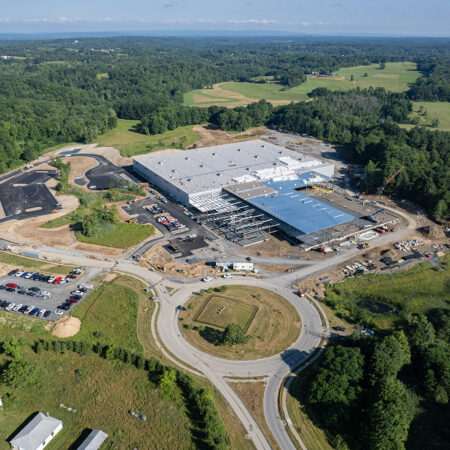 Aerial view: large industrial building construction amid trees, roundabout.