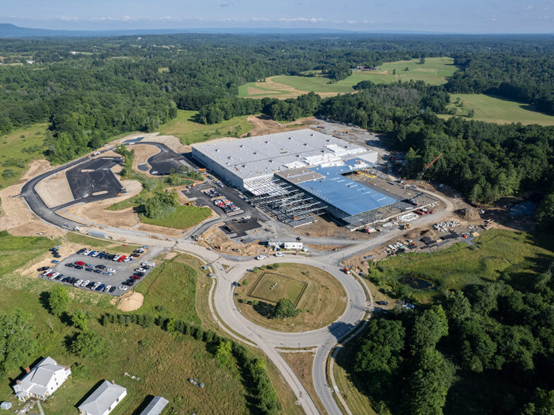 Aerial view: large industrial building construction amid trees, roundabout.