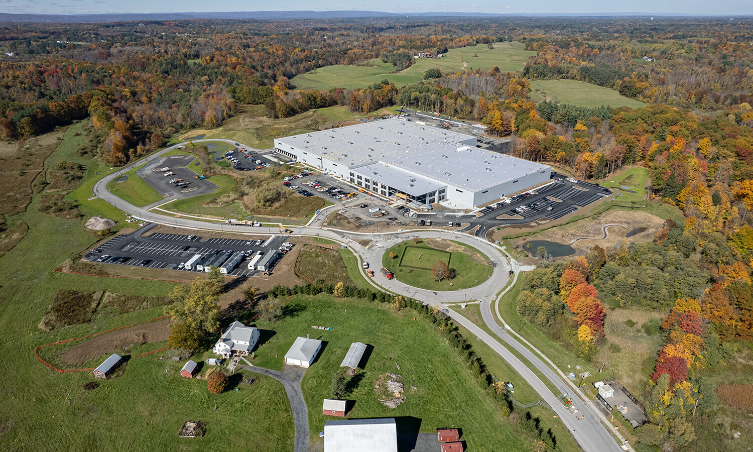 Aerial view: large warehouse, parking lots, rural fall landscape.