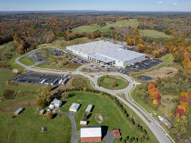 Aerial view: large warehouse, parking lots, rural fall landscape.