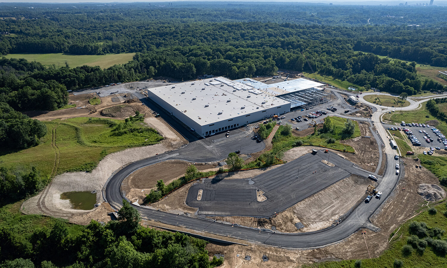 Aerial view: industrial building under construction, forest in background.