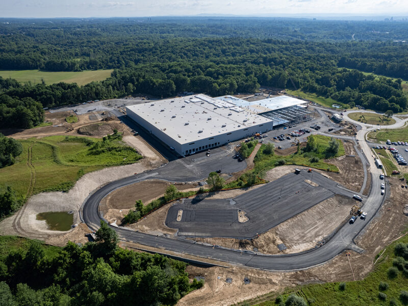 Aerial view: industrial building under construction, forest in background.